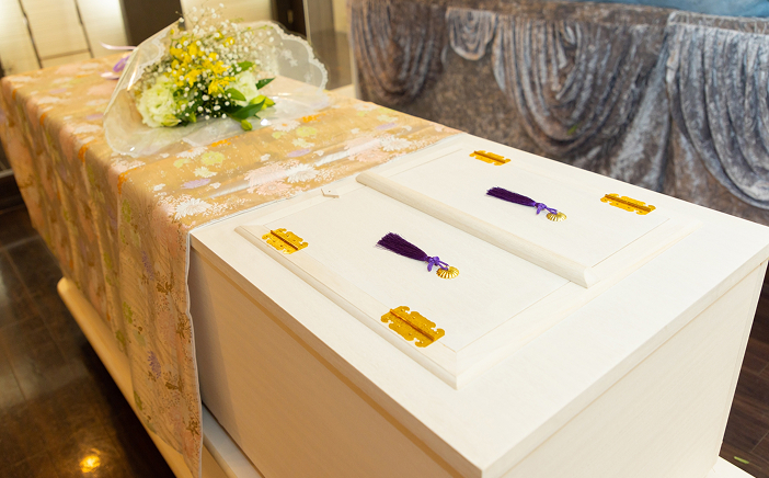 白い棺の上に飾られた生花と紫・金色の装飾品