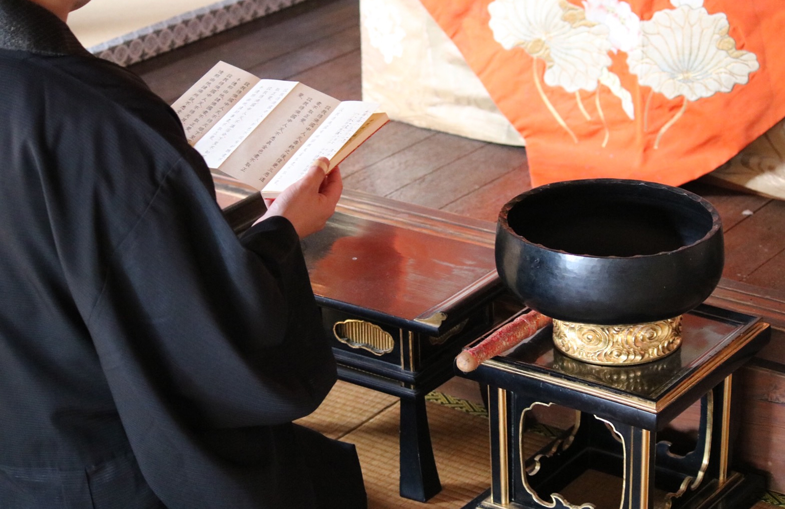 僧侶が経本を手に取り読経を行っている様子、前には鈴が置かれている