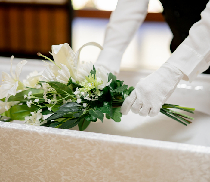 白い手袋をつけた手で持つ白百合とカスミソウの小さな花束