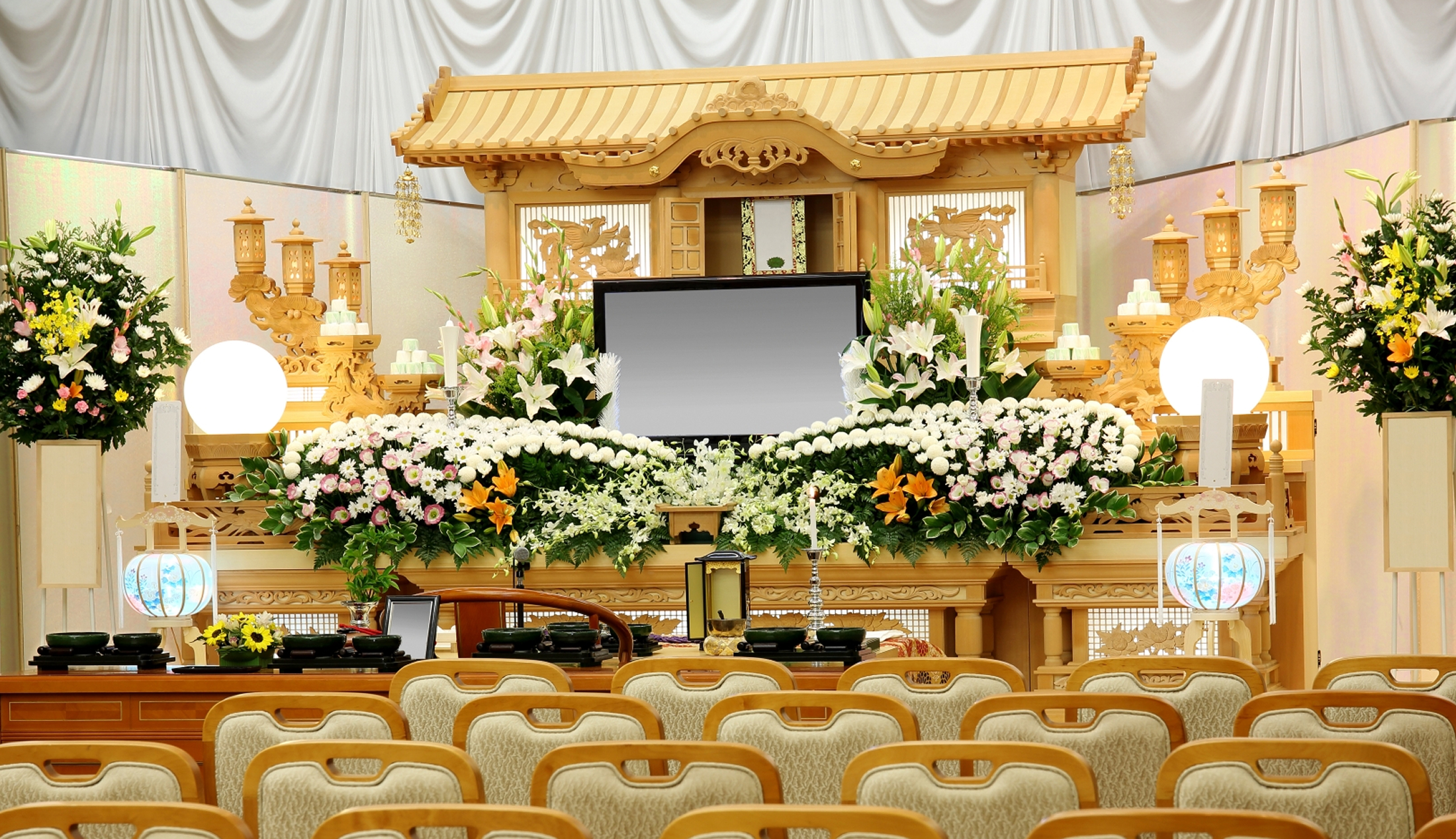 白い菊や色とりどりの供花で飾られた祭壇と、整然と並べられた椅子が配置された葬儀式場