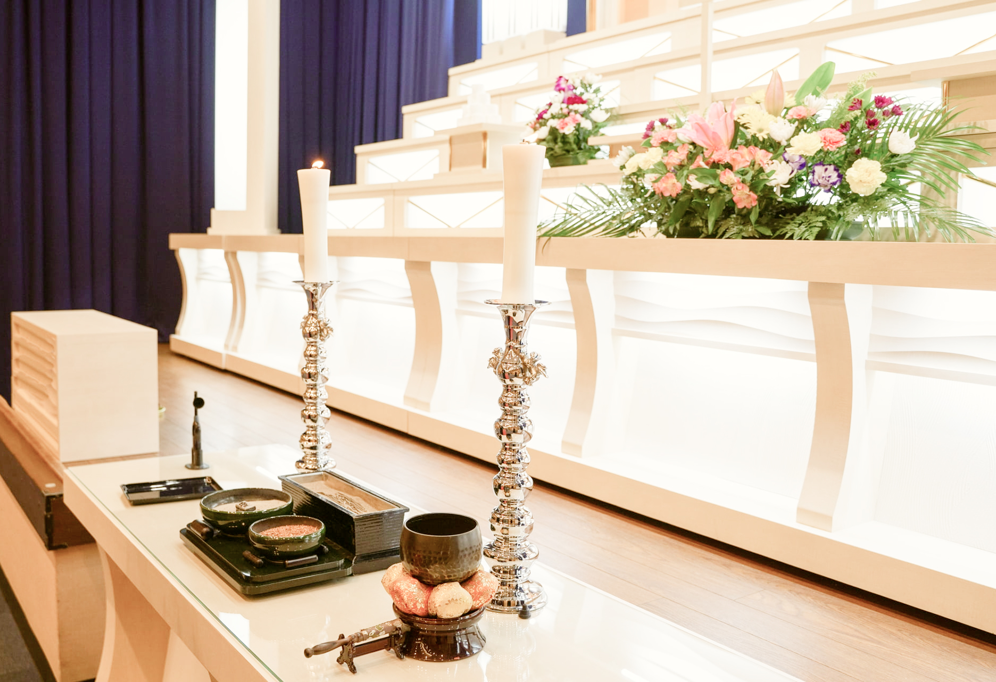 白木の祭壇と供花、ろうそくが並ぶ葬儀会場